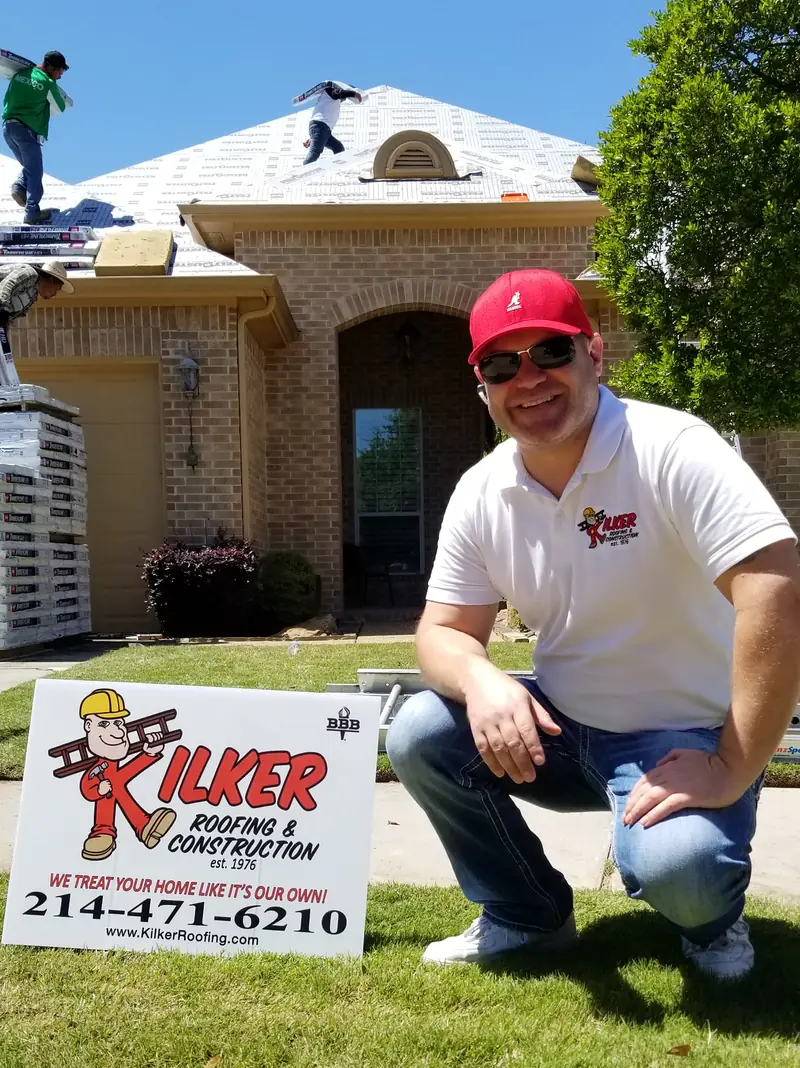 Derik Kilker kneeling by a Kilker Roofing yard sign at a finished job